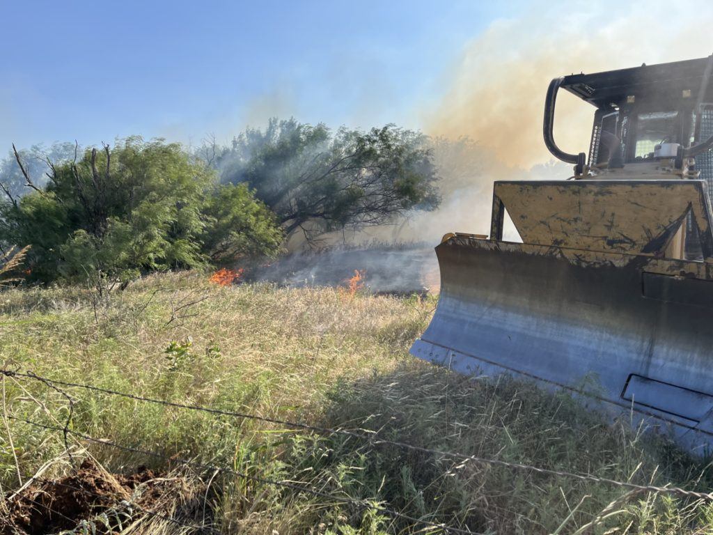 a tractor sits in a field as a fire burns in the background