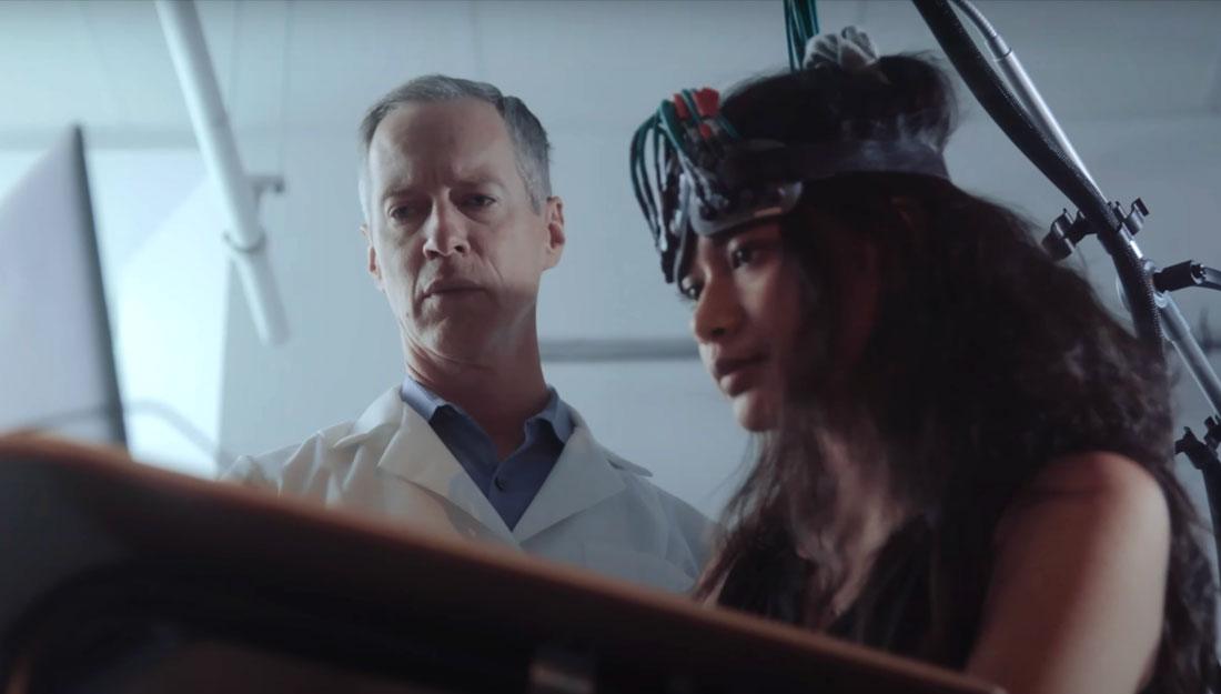 researcher standing next to a young woman wearing a headset as part of ergonomics research