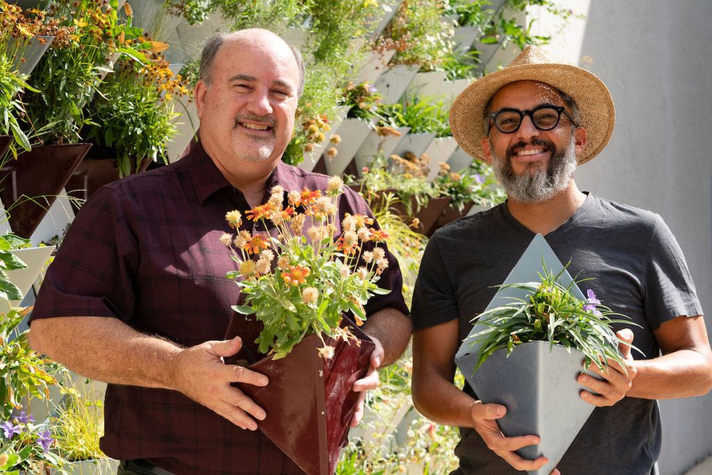 a photo of two men standing in front of the langford living wall smiling, each holding one of the metal planters