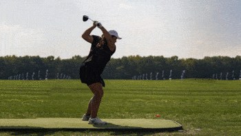 a photo of a young woman about to swing a driver at an orange golf ball on a tee