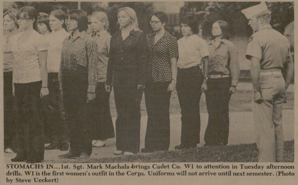a newspaper clip with a photo of women in casual clothing standing at attention while a man in a corps of cadets uniform give them instructions