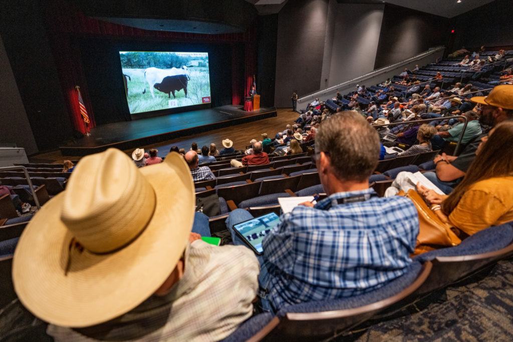 View from the crowd of a teaching theater full of seated participants looking down toward the stage
