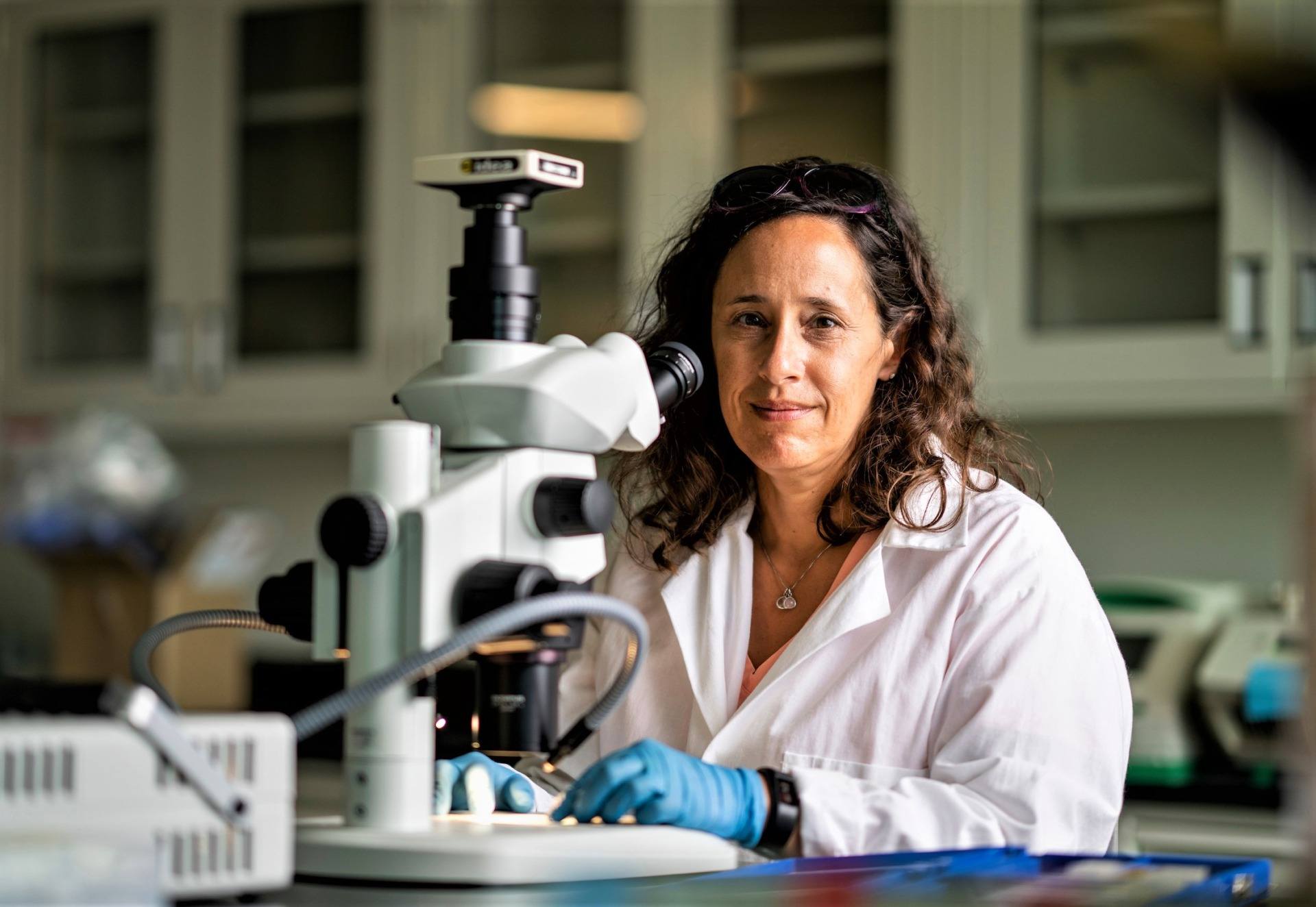 Portrait of Jessica Light seated in lab in front of a microscope