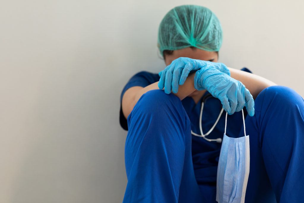 a health care worker sitting on the floor with their head and arms resting on their knees