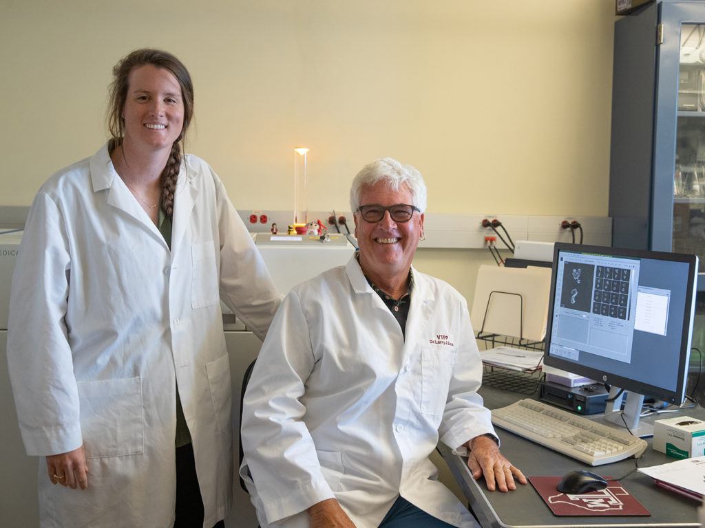 portrait of female student standing next to a seated professor, both wearing white lab coats