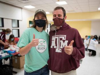 a photo of a man and a woman in casual clothing and medical masks standing next to each other giving the thumbs up