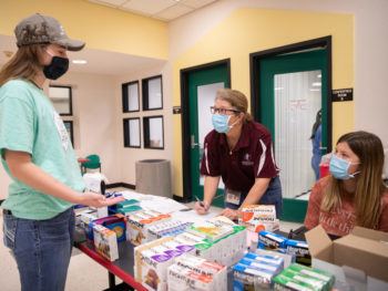 a photo of three women in casual clothes and medical masks standing around a table filled with medicine for pets