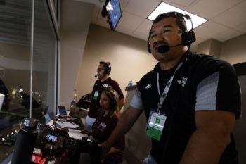 A close-up photo of a standing man wearing headphones looking out over the game