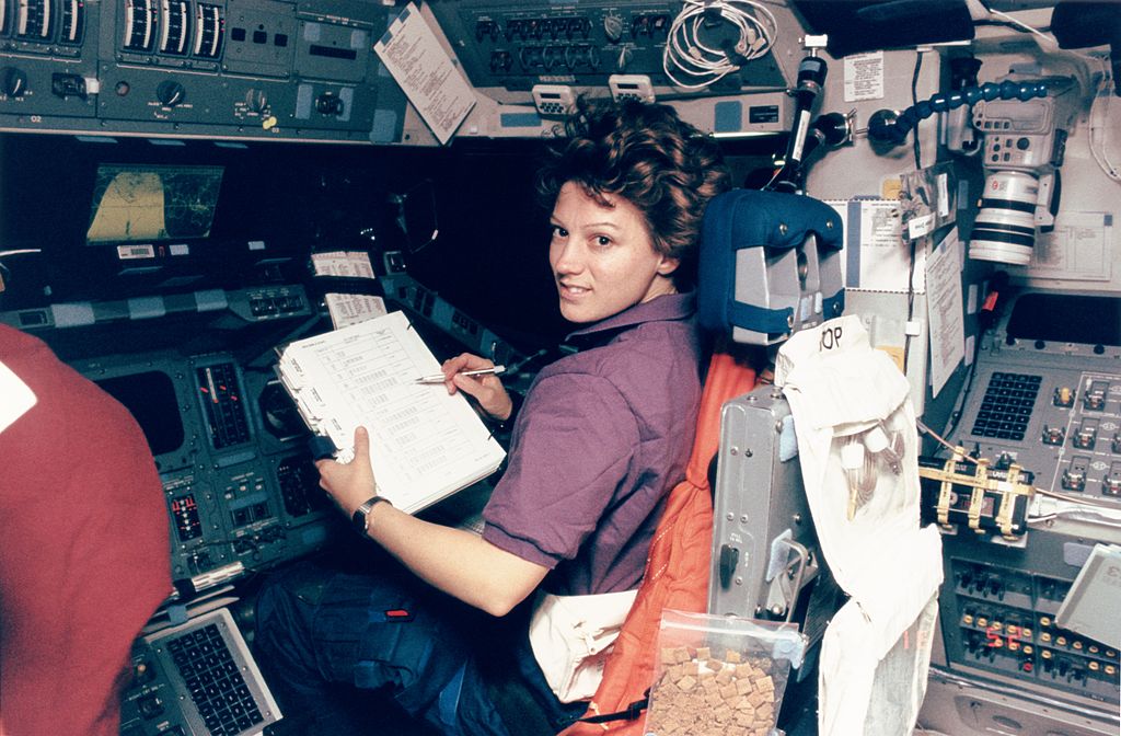 archival photo of astronaut eileen collins sitting down inside a space shuttle