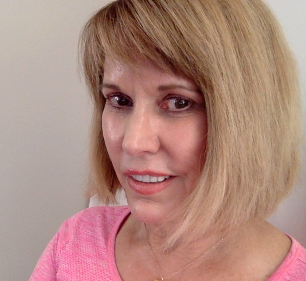 a photo of a woman in a pink shirt looking at the camera and smiling slightly