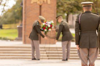 A cadet watches on as two cadets in the background set up a wreath in front of the Corps arches on campus
