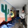 a photo of two young women removing tape from a painted mural inside a shipping container clinic