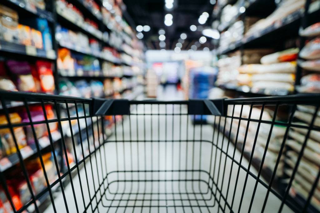 eye-level perspective of a shopping cart in the middle of a grocery store aisle