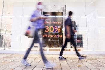 a photo of two blurry people walking past a storefront with a large "black friday - 30% off everything" sign in the window