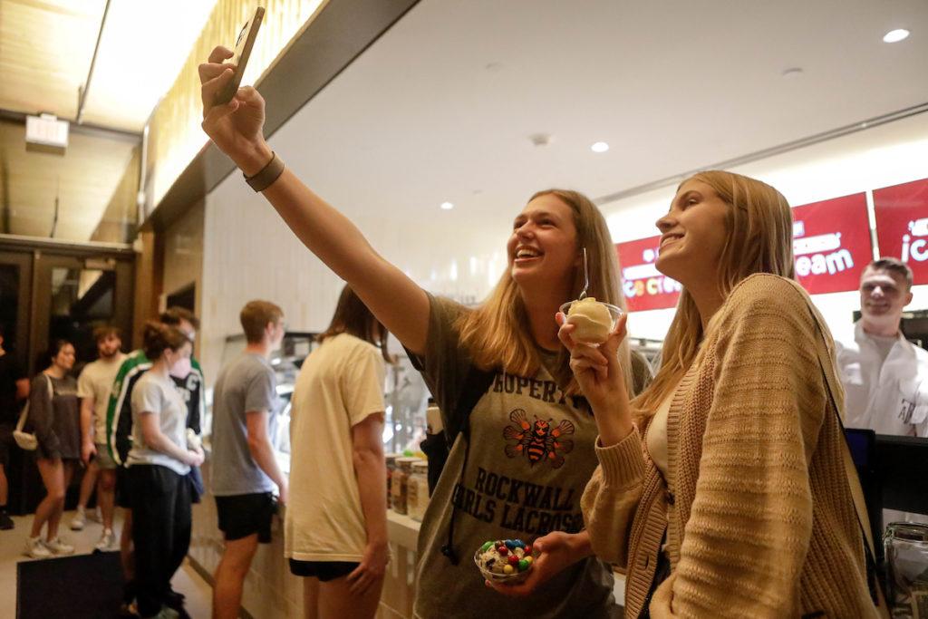 Two female students hold up a cell phone as they pose for a selfie inside the creamery