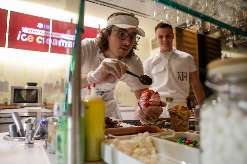 A Yell Leader looks on as an employee spoons strawberry syrup and other toppings onto a sundae
