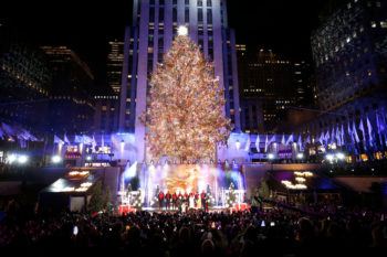 Photo taken at the 2022 Rockefeller Center Christmas Tree lighting, with performers on a stage below the tree