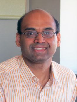 a headshot of a man in a white and orange striped shirt and glasses