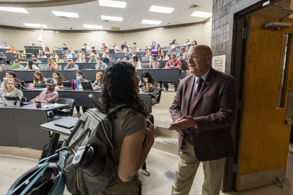 Jeffrey Savell stands at the front of a teaching theater filled with students speaking to a young woman wearing a backpack
