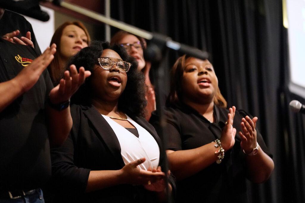 a photo of a group of people wearing black, clapping their hands, and singing