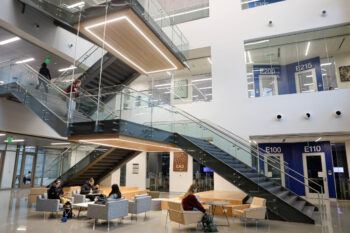 a photo of a big staircase in the center of a room. The underside of each landing has a glowing rectangle on it, casting light on the stairs and study spaces below.