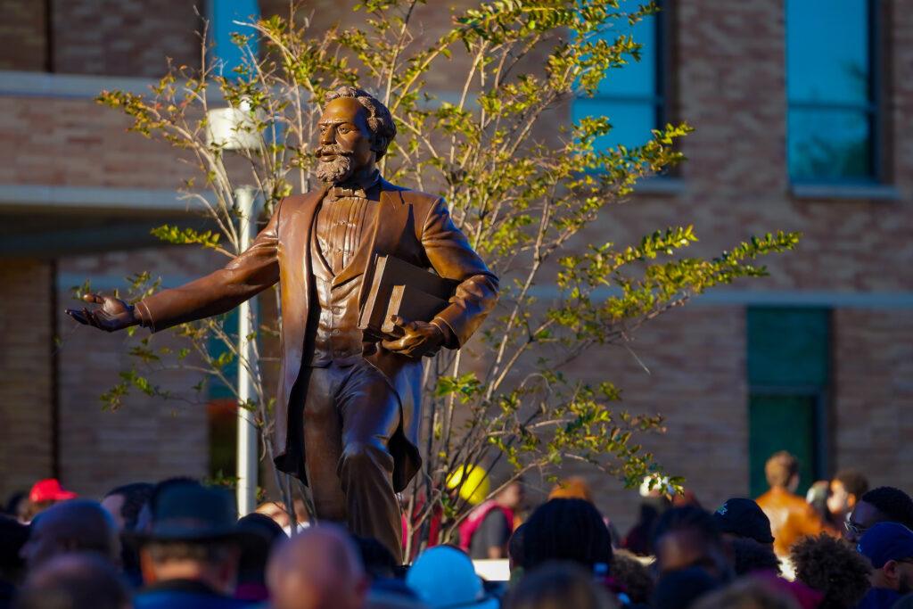 a photo of the tops of peoples heads looking at the statue of Matthew Gaines