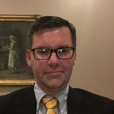 a headshot of a man in a suit and glasses
