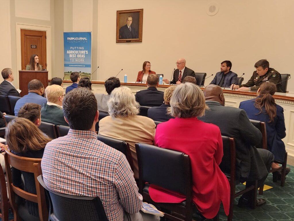 a photo of a group of people watching a panel of speakers, with Texas A&M professor Edwin Price speaking into a microphone