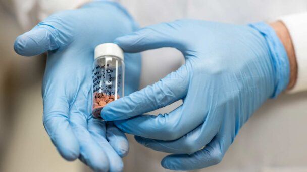 Close-up photo of two gloved hands holding a small vial of medication
