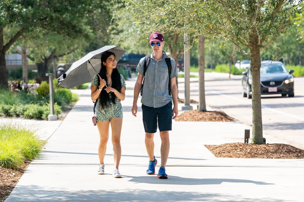 a photo of a young woman holding an umbrella walking next to a man in a maroon baseball cap