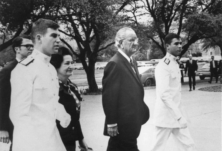 a photo of Lady Bird and Lyndon Johnson accompanied by cadets in Ross Volunteer uniforms walking across the Texas A&M campus.