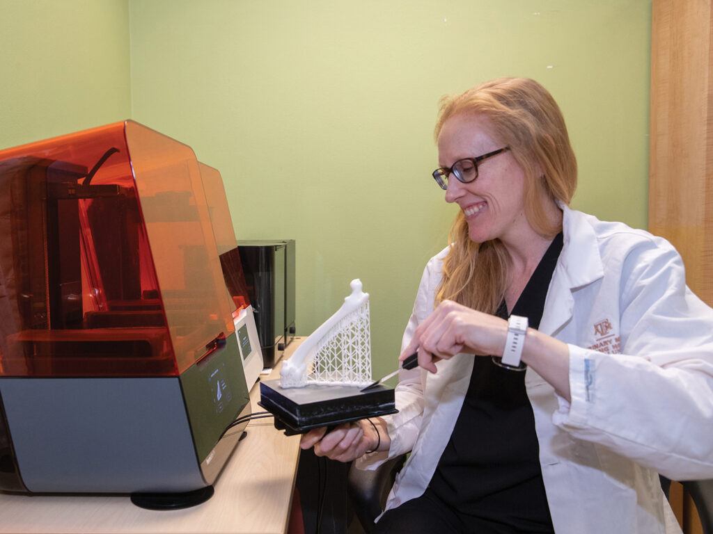 Barnes removes a newly printed 3D model and its scaffolding (connecting the printed bone to the platform) from the printer’s build platform (black). Once removed from the platform, the bone model is detached from the scaffolding.