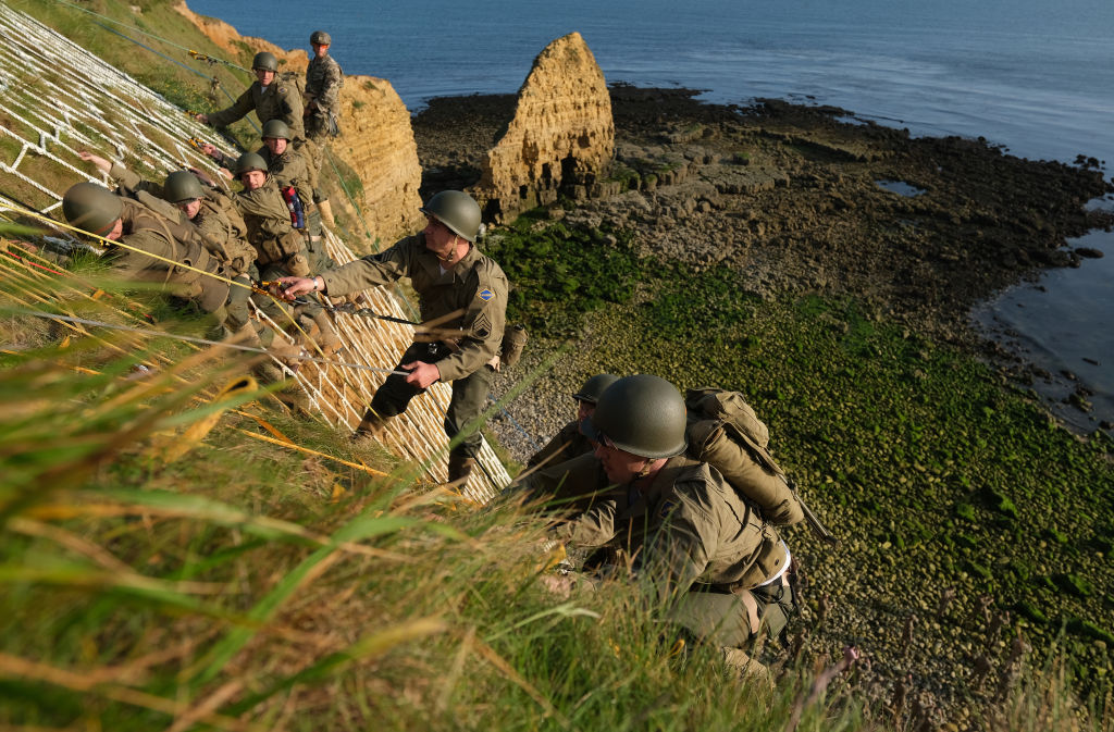 a photo of modern army rangers in WWII uniforms recreating the famous ascent up the cliffs at pointe du hoc