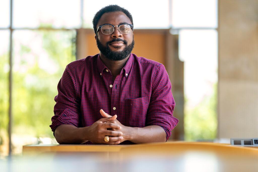 Portrait of Jeffery Boakye seated at a table with his arms clasped in front of him
