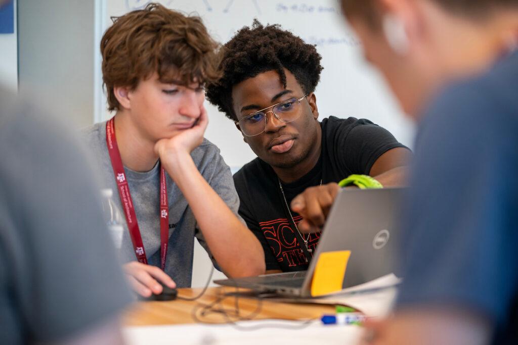 two students look at a laptop screen on a table
