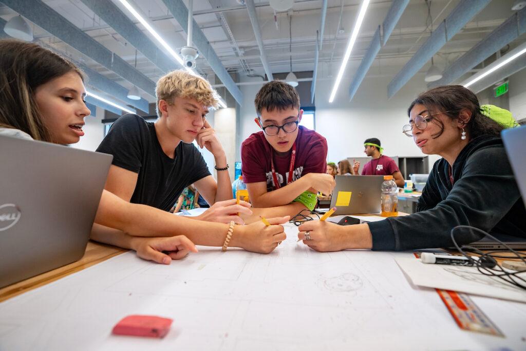 a photo of a group of students huddled around a table drawing architectural plans
