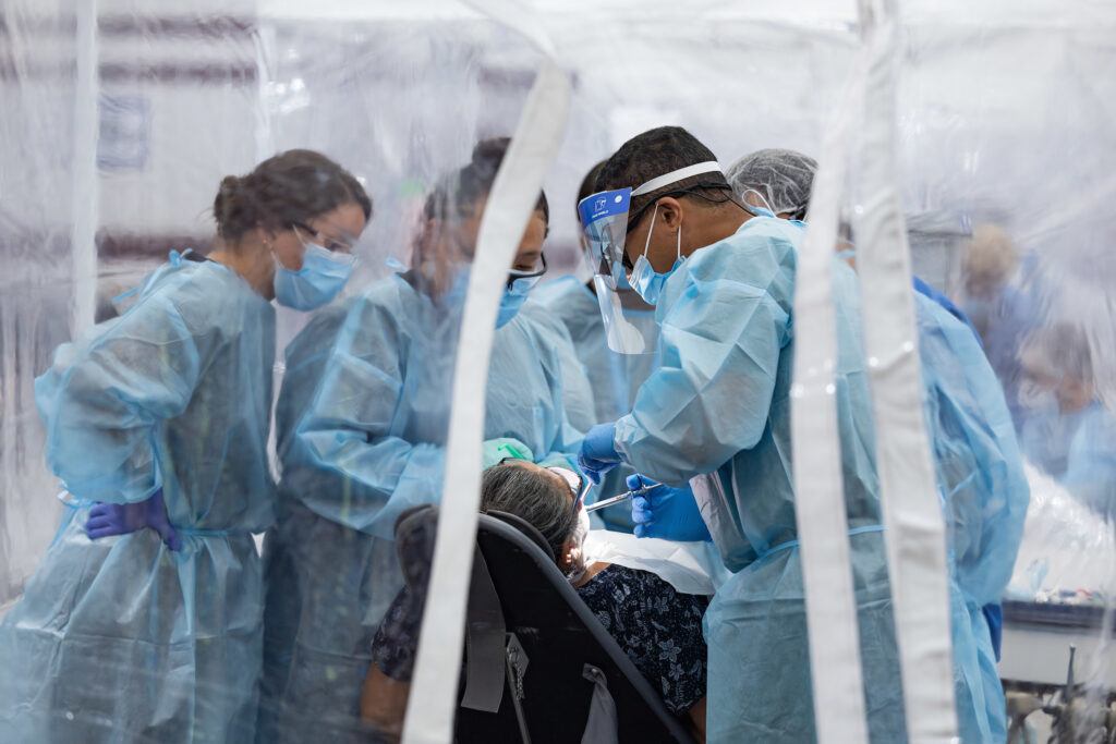 a group of several people in scrubs tending to a dental patient in a plastic tent