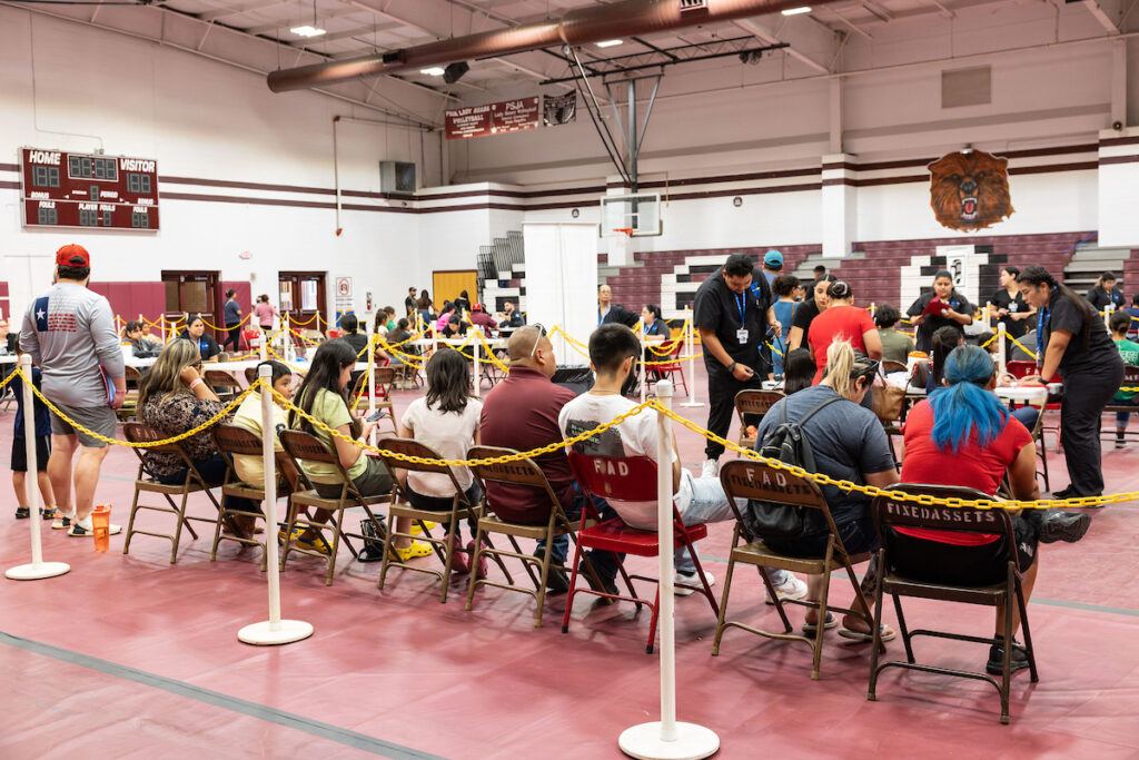 a photo of a row of people sitting on metal folding chairs in a gymnasium