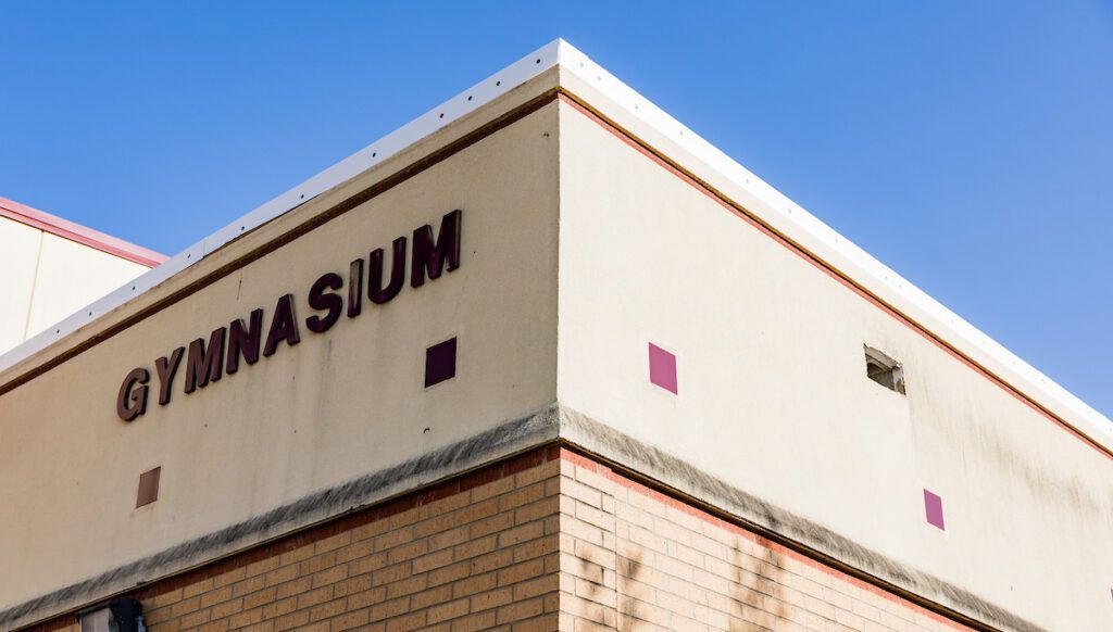 a photo of the corner of a building with letters spelling out "GYMNASIUM" affixed to one side