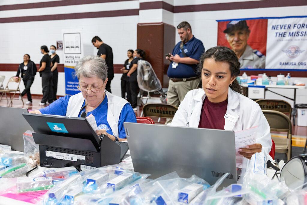 a photo of a young woman in a maroon shirt and lab coat sitting at a table working