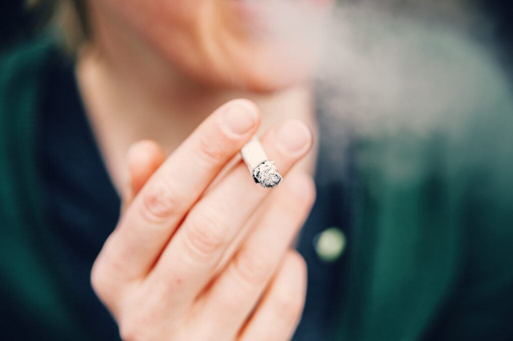 Unrecognizable woman wrapped in cigarette smoke holding a lit cigarette in her hand