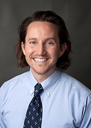 a headshot of a man with shoulder length hair in a blue shirt and tie