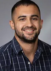 a headshot of a man with short dark hair in a checkered dark blue shirt