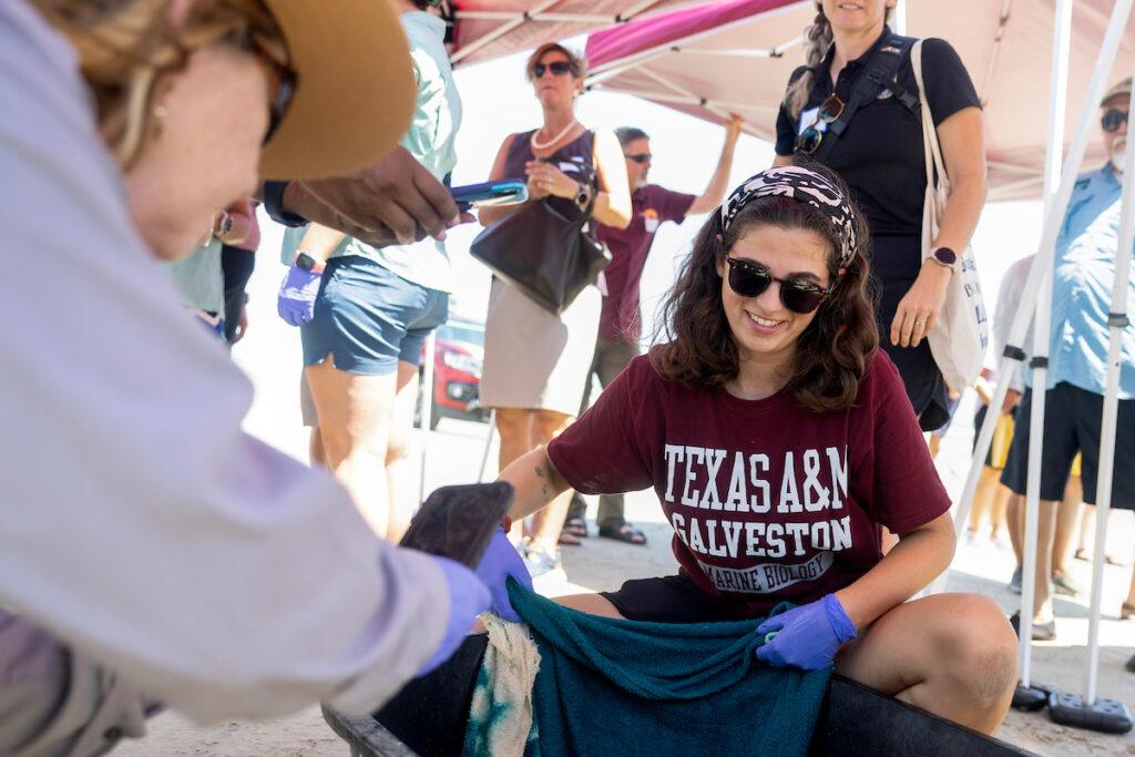 a photo of a young woman in sunglasses holding up a wet towel while a woman in a national parks uniform takes a photo on her iphone