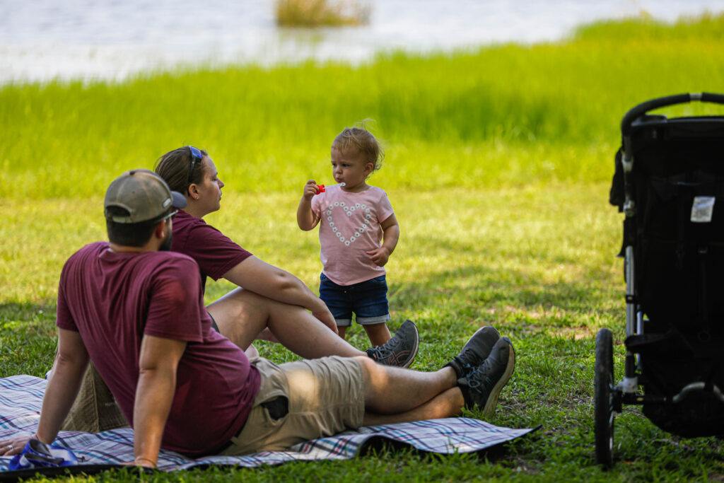 A photo of a young family on the grass near a lake.