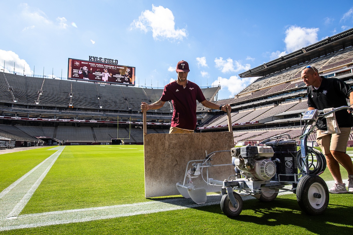 Two men using a machine to paint white lines on the field