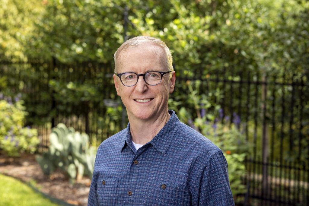 A photo of a man standing outdoors in a landscaped yard.
