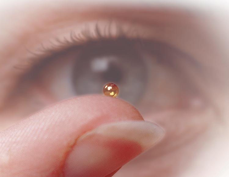 An inertial confinement fusion fuel microcapsule being held on a person's finger in front of their eye to show its tiny size