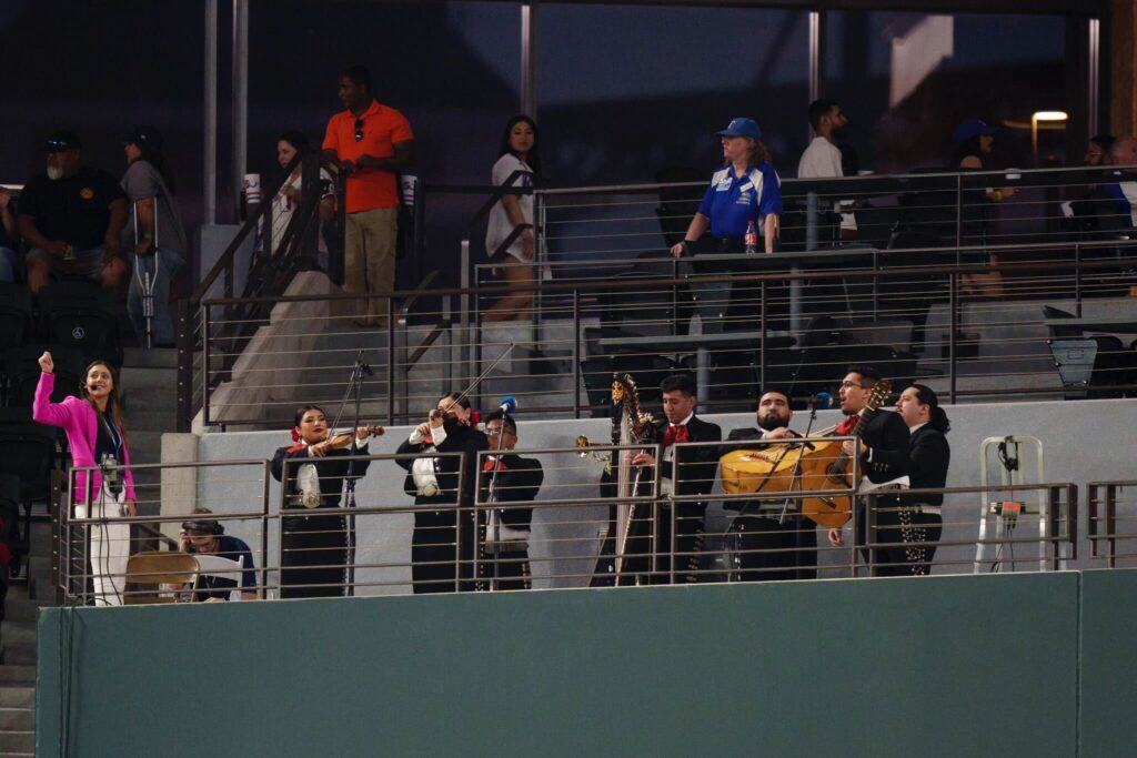 a photo of a woman in a pink blazer next to a mariachi band in a baseball stadium