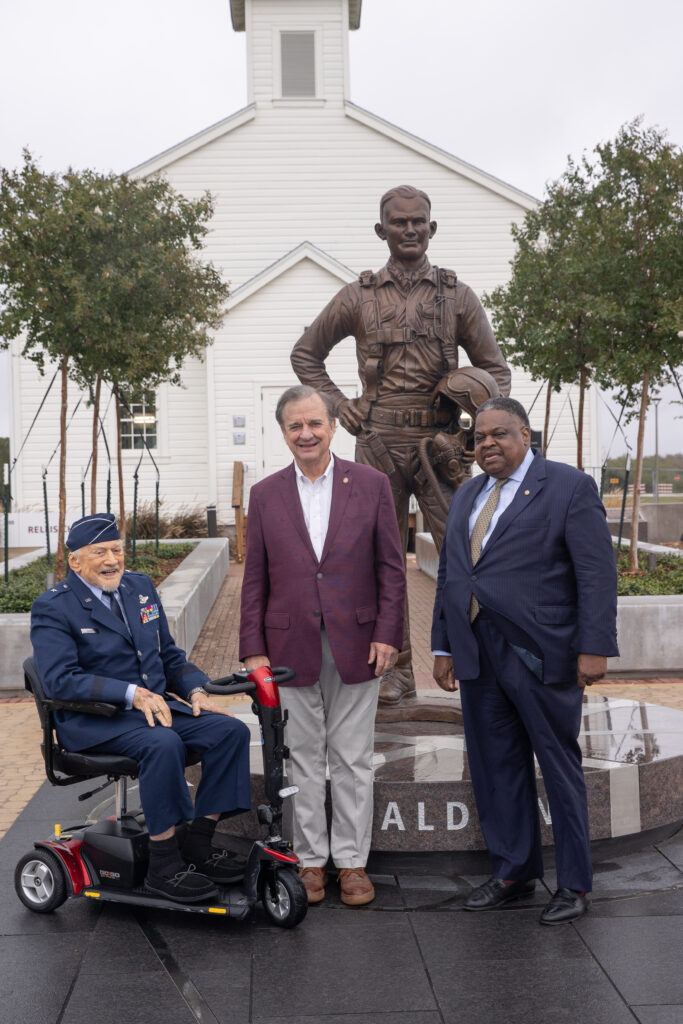 A photo of three men posing for a photo in front of a bronze statue.